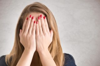 両手で顔を隠す赤いマニキュアをつけた女性