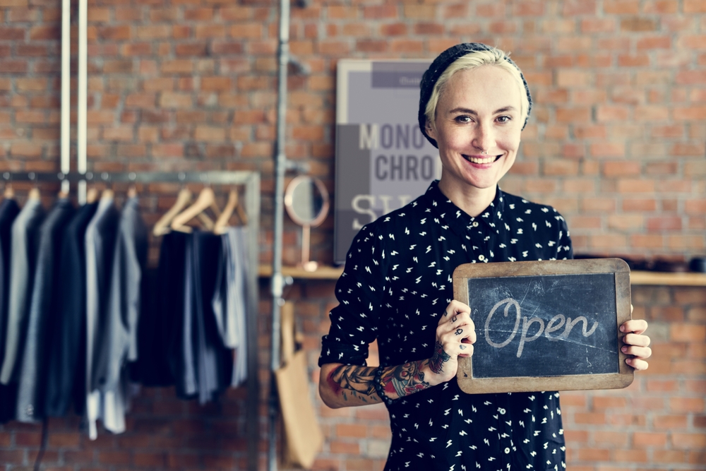 「Open」と書かれた黒板を持つ、アパレルの店で働く女性
