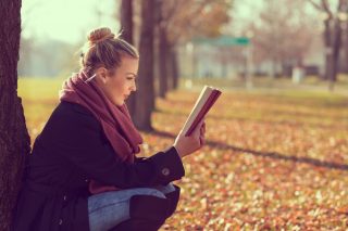 秋の公園でしゃがみながら本を読む女性